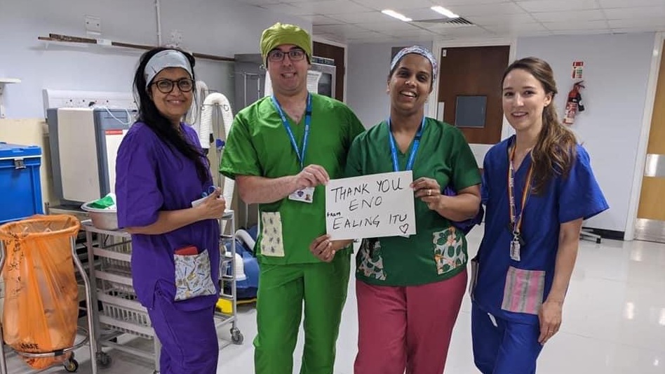 NHS workers wearing colourful scrubs and smiling, and holding up a sign reading "thank you English National Opera"