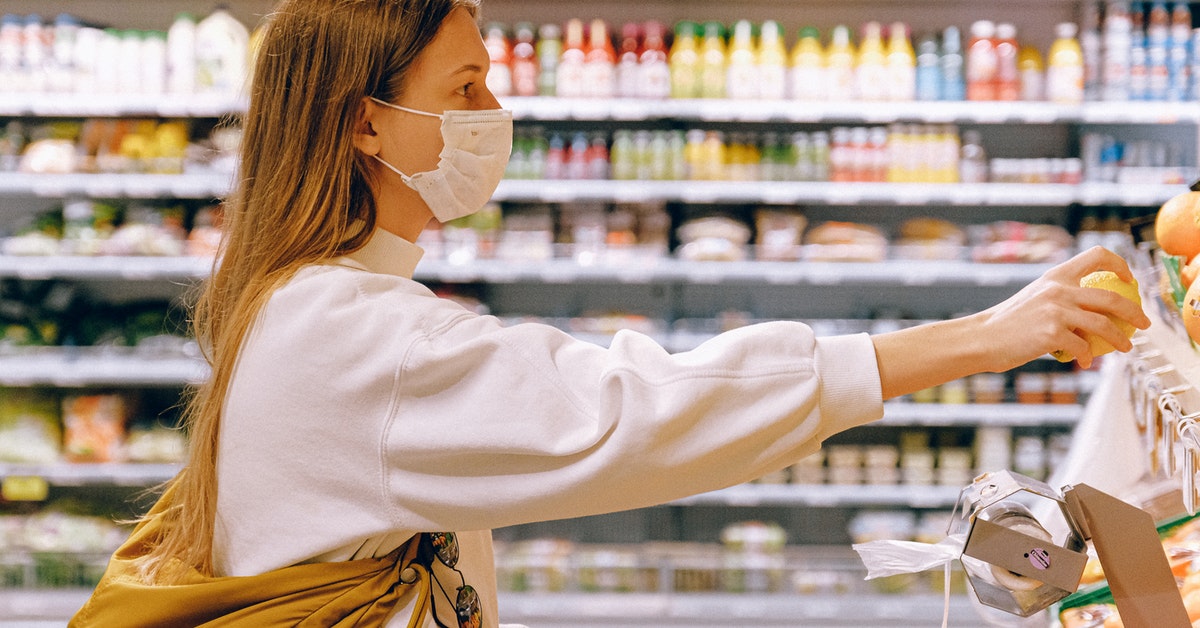 Woman picking out oranges from a local supermarket wearing a mask.